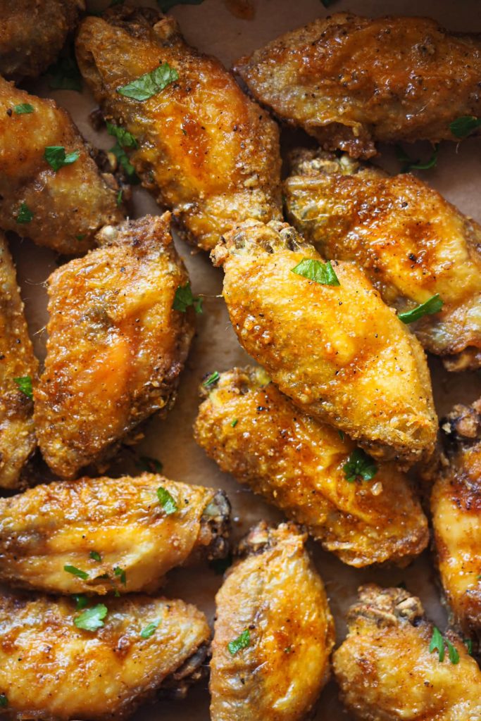 Alitas de pollo crujientes al horno adictivas. Llevan un aliño de ajo y pimentón que es, literal, para chuparse los dedos y van acompañadas de un dip de yogur y limón que balancea todos los sabores. Aquí se ven las alitas de cerca con perejil picado espolvoreado por encima.