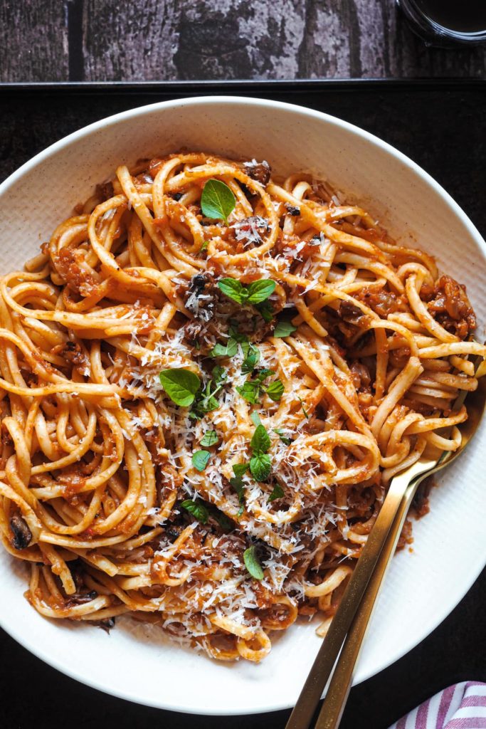 No tienes que ser vegetariano ni vegano para enamorarte de estos Espaguetis con Boloñesa de Coliflor, porque es tan sustanciosa que solo por el sabor y texturas ya te quedarás boqueabierto. Es una receta perfecta para introducir un poco de verduritas a la dieta sin uno darse cuenta. ¿Y que tienes una cena con amigos veganos? ¡Pues esta es la tuya para triunfar! En esta foto se ve un plato de espaguetis con boloñesa de coliflor y decorados con parmesano y orégano.