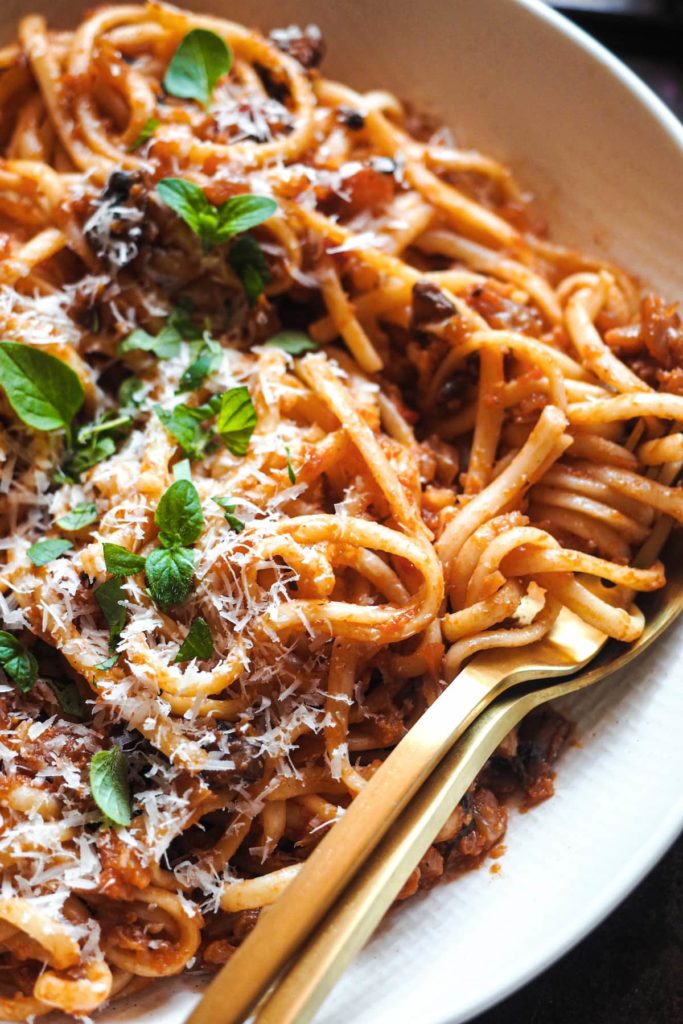 No tienes que ser vegetariano ni vegano para enamorarte de estos Espaguetis con Boloñesa de Coliflor, porque es tan sustanciosa que solo por el sabor y texturas ya te quedarás boqueabierto. Es una receta perfecta para introducir un poco de verduritas a la dieta sin uno darse cuenta. ¿Y que tienes una cena con amigos veganos? ¡Pues esta es la tuya para triunfar! En esta foto se ve un plato de espaguetis con boloñesa de coliflor y decorados con parmesano y orégano.