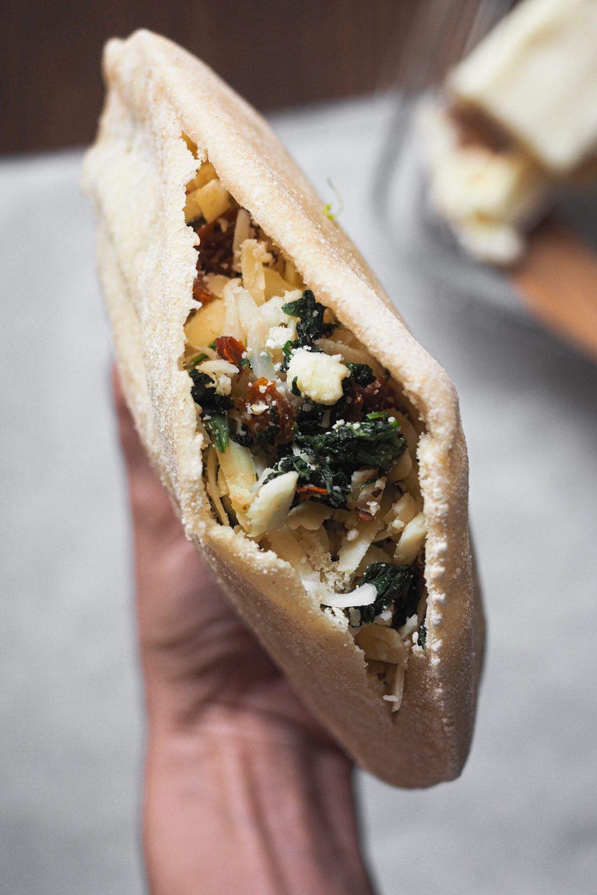 Delicioso pan pita relleno de espinacas, queso y tomate seco para un bocadillo planchado diferente. El pita está sujetado con la mano de forma que se ve la abertura con el relleno de cerca.