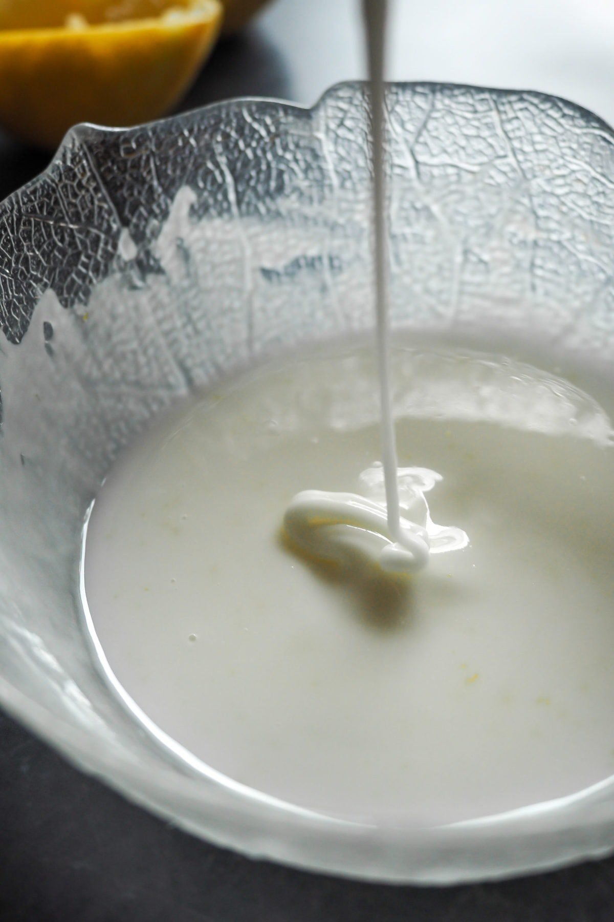 Glaseado de Limón recién preparado. Un hilo de glaseado cae encima del resto de glaseado en un bol. | Receta de Paula's Apron