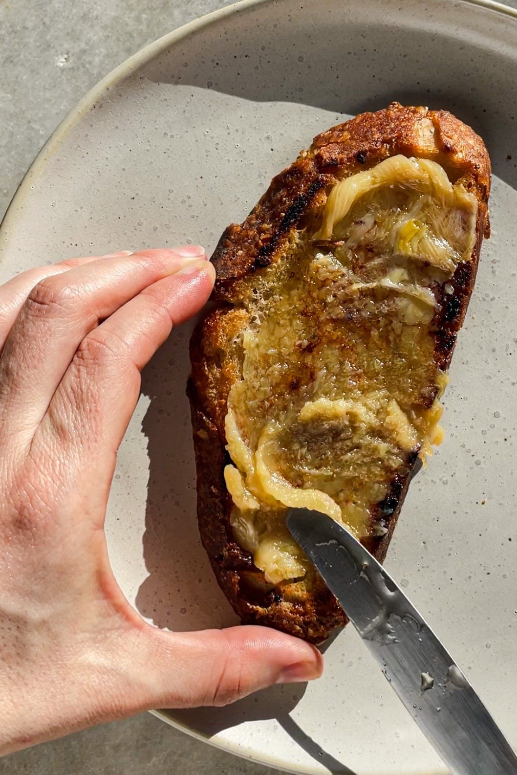 Esta receta de Ajos Confitados (o Confit de Ajo) se va a convertir en tu nuevo indispensable en la cocina porque es tan fácil y los ajos confitados son taaaaaan espectaculares y versátiles. Solo necesitas unas cuantas cabezas de ajo, tus especias y hierbas favoritas, mucho aceite de oliva y 30 minutos. El resultado es un ajo que se deshace como mantequilla, con un sabor dulzón y que puedes usar de mil maneras. Aquí por ejemplo lo vemos untado en una tostada y es que así de simple ya está de muerte. Además, como bonus te queda un aceite de ajo insuperable. | Receta de Paula's Apron