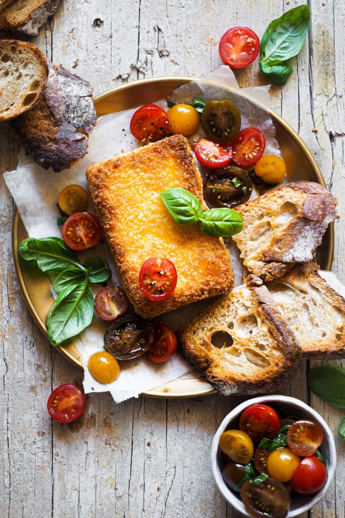 Este Feta Rebozado con Tomates Cherry es un aperitivo perfecto. El queso feta está rebozado con panko para que quede extra crujiente y va acompañado de una ensalada de tomate y albahaca que casa con el queso a la perfección. Sírvelo con tu pan favorito y un poco de miel para contrastar con el feta salado y, voilà, ¡un aperitivo rápido listo para ser devorado! | Receta de Paula's Apron