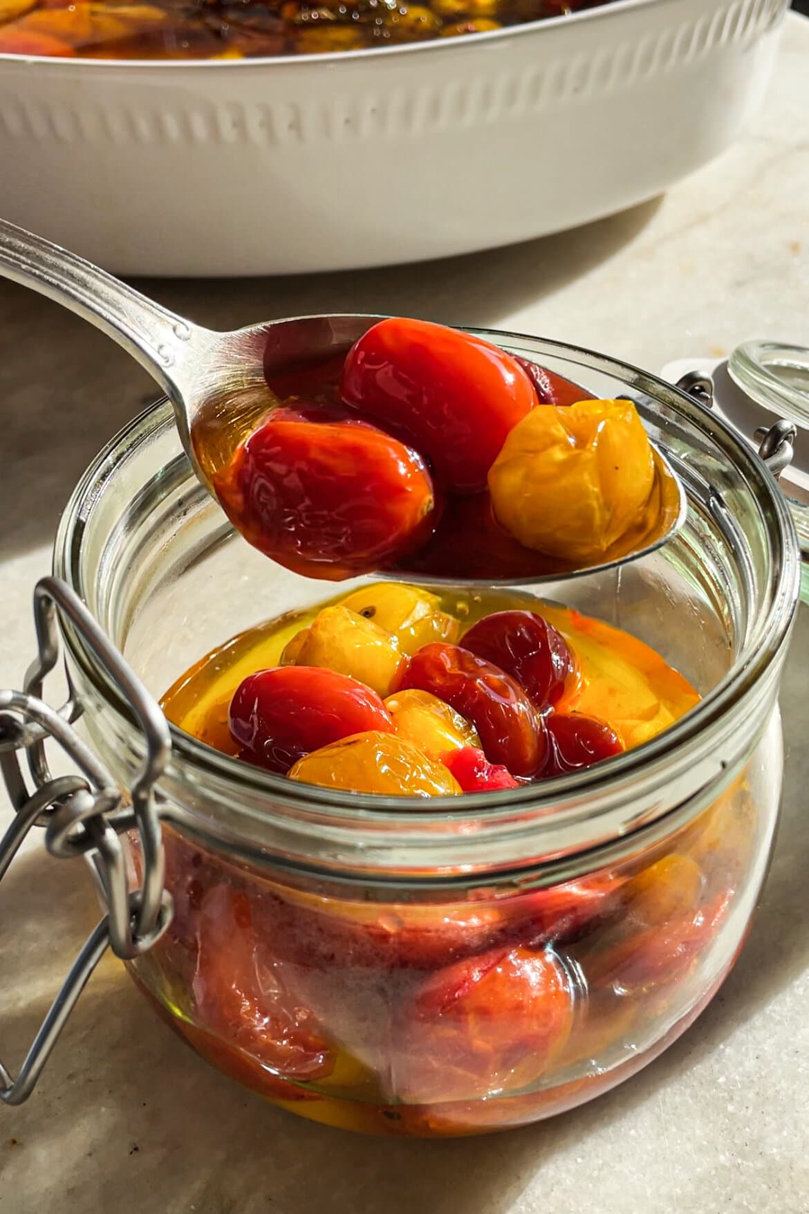 El Tomate Confitado (o Confit de Tomate) es mi forma favorita de conservar el verano. Solo necesitas 5 minutos como máximo de preparación y el resto lo hace el horno. El resultado es un tomate potenciado de sabor, jugoso y dulzón ideal para dar un toque especial y alegrar una infinidad de platos. Lo puedes usar sobre tostadas, con pasta, como topping de untables, carne, pescado, en bocadillos… Hoy le he añadido chalotas, ajo y tomillo pero puedes usar los aromatizantes que más te gusten. En cualquier caso, el aceite infusionado que te va a quedar será delicioso y podrás aprovechar hasta la última gota. | Receta de Paula's Apron