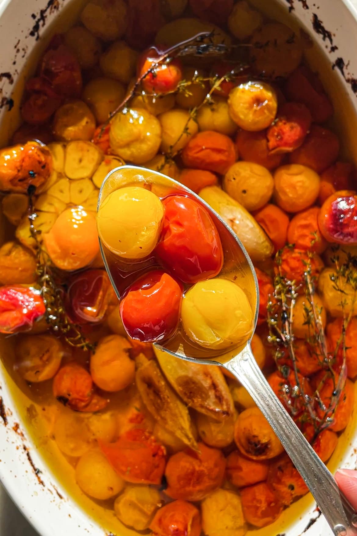 El Tomate Confitado (o Confit de Tomate) es mi forma favorita de conservar el verano. Solo necesitas 5 minutos como máximo de preparación y el resto lo hace el horno. El resultado es un tomate potenciado de sabor, jugoso y dulzón ideal para dar un toque especial y alegrar una infinidad de platos. Lo puedes usar sobre tostadas, con pasta, como topping de untables, carne, pescado, en bocadillos… Hoy le he añadido chalotas, ajo y tomillo pero puedes usar los aromatizantes que más te gusten. En cualquier caso, el aceite infusionado que te va a quedar será delicioso y podrás aprovechar hasta la última gota. | Receta de Paula's Apron