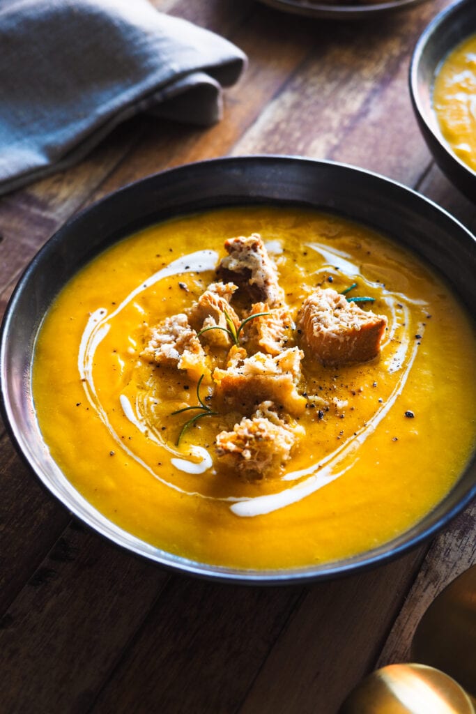 Esta Crema de Calabaza Asada con Picatostes de Gruyère es sencilla, todo se hace en una bandeja de horno y el asar las verduras hace que quede extra cremosa y con un plus de sabor. Como topping lleva unos picatostes con gruyère que no solo le dan un contrapunto crujiente, sino que además el toque salado del queso balancea el dulzor de la calabaza. En resumen, es un primero nutritivo y saludable perfecto para otoño e invierno.| Receta de Paula's Apron