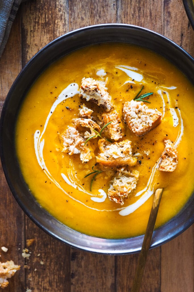 Esta Crema de Calabaza Asada con Picatostes de Gruyère es sencilla, todo se hace en una bandeja de horno y el asar las verduras hace que quede extra cremosa y con un plus de sabor. Como topping lleva unos picatostes con gruyère que no solo le dan un contrapunto crujiente, sino que además el toque salado del queso balancea el dulzor de la calabaza. En resumen, es un primero nutritivo y saludable perfecto para otoño e invierno.| Receta de Paula's Apron