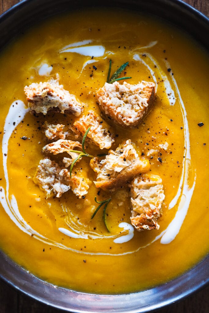 Esta Crema de Calabaza Asada con Picatostes de Gruyère es sencilla, todo se hace en una bandeja de horno y el asar las verduras hace que quede extra cremosa y con un plus de sabor. Como topping lleva unos picatostes con gruyère que no solo le dan un contrapunto crujiente, sino que además el toque salado del queso balancea el dulzor de la calabaza. En resumen, es un primero nutritivo y saludable perfecto para otoño e invierno.| Receta de Paula's Apron