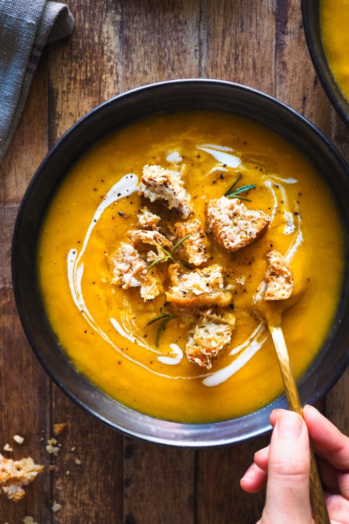 Esta Crema de Calabaza Asada con Picatostes de Gruyère es sencilla, todo se hace en una bandeja de horno y el asar las verduras hace que quede extra cremosa y con un plus de sabor. Como topping lleva unos picatostes con gruyère que no solo le dan un contrapunto crujiente, sino que además el toque salado del queso balancea el dulzor de la calabaza. En resumen, es un primero nutritivo y saludable perfecto para otoño e invierno.| Receta de Paula's Apron