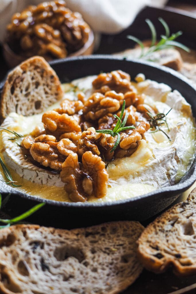 Esta receta de camembert al horno con ajo, romero y nueces caramelizadas es festiva, fácil de preparar y ¡siempre enamora! Rápida, pocos ingredientes y súper deliciosa. El ajo y romero aportan un aroma increíble al Camembert, ya de por si un poco frutal y complejo. Para acompañar, unas tostadas y la guinda del pastel, unas nueces caramelizadas con sirope de arce que también puedes usar para dipear o como acompañamiento de cualquier tabla de quesos y embutidos. | Receta de Paula's Apron