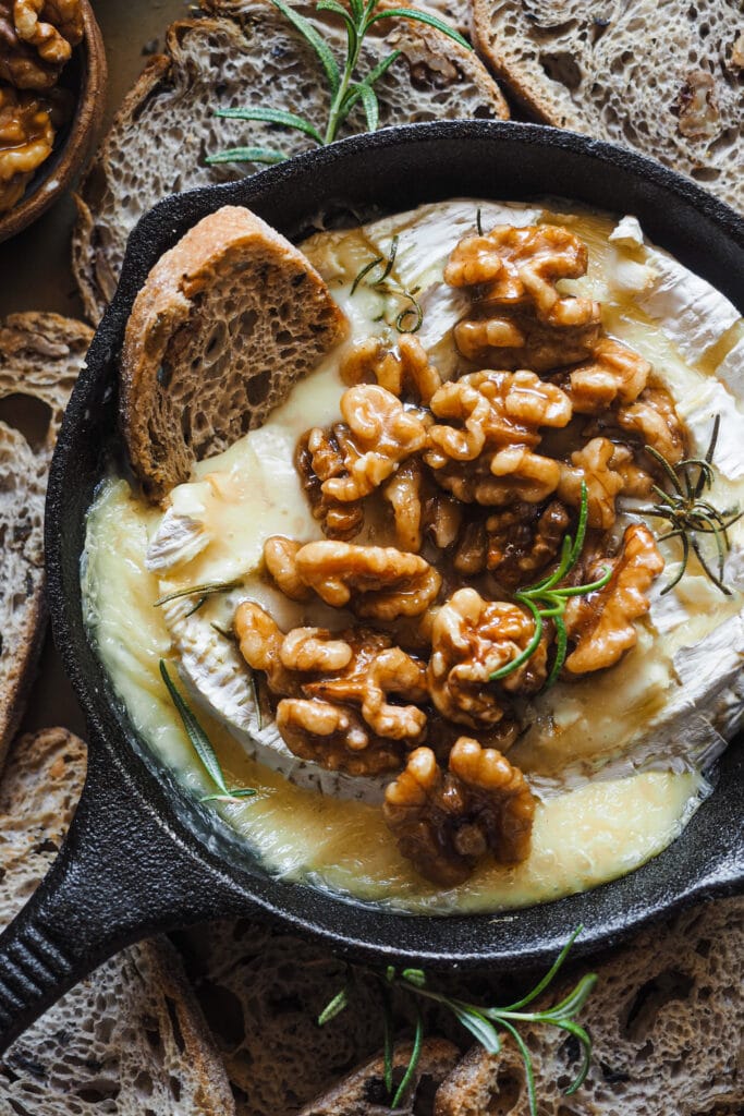 Esta receta de camembert al horno con ajo, romero y nueces caramelizadas es festiva, fácil de preparar y ¡siempre enamora! Rápida, pocos ingredientes y súper deliciosa. El ajo y romero aportan un aroma increíble al Camembert, ya de por si un poco frutal y complejo. Para acompañar, unas tostadas y la guinda del pastel, unas nueces caramelizadas con sirope de arce que también puedes usar para dipear o como acompañamiento de cualquier tabla de quesos y embutidos. | Receta de Paula's Apron