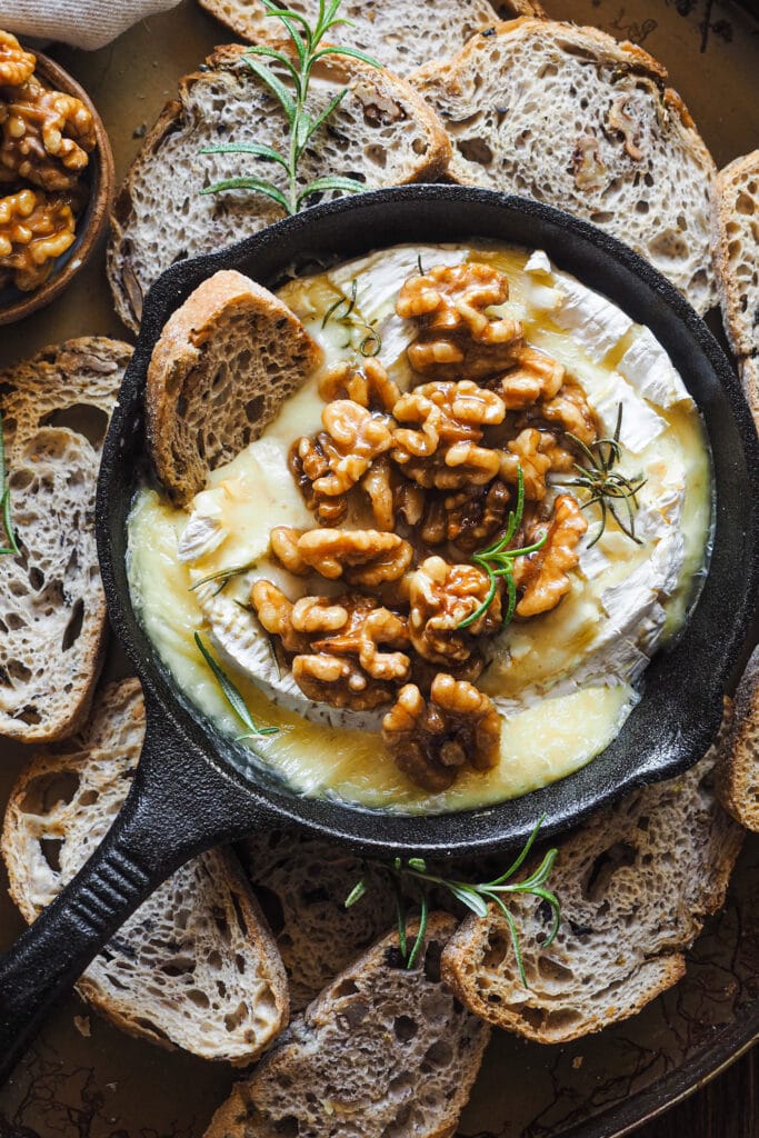 Esta receta de camembert al horno con ajo, romero y nueces caramelizadas es festiva, fácil de preparar y ¡siempre enamora! Rápida, pocos ingredientes y súper deliciosa. El ajo y romero aportan un aroma increíble al Camembert, ya de por si un poco frutal y complejo. Para acompañar, unas tostadas y la guinda del pastel, unas nueces caramelizadas con sirope de arce que también puedes usar para dipear o como acompañamiento de cualquier tabla de quesos y embutidos. | Receta de Paula's Apron