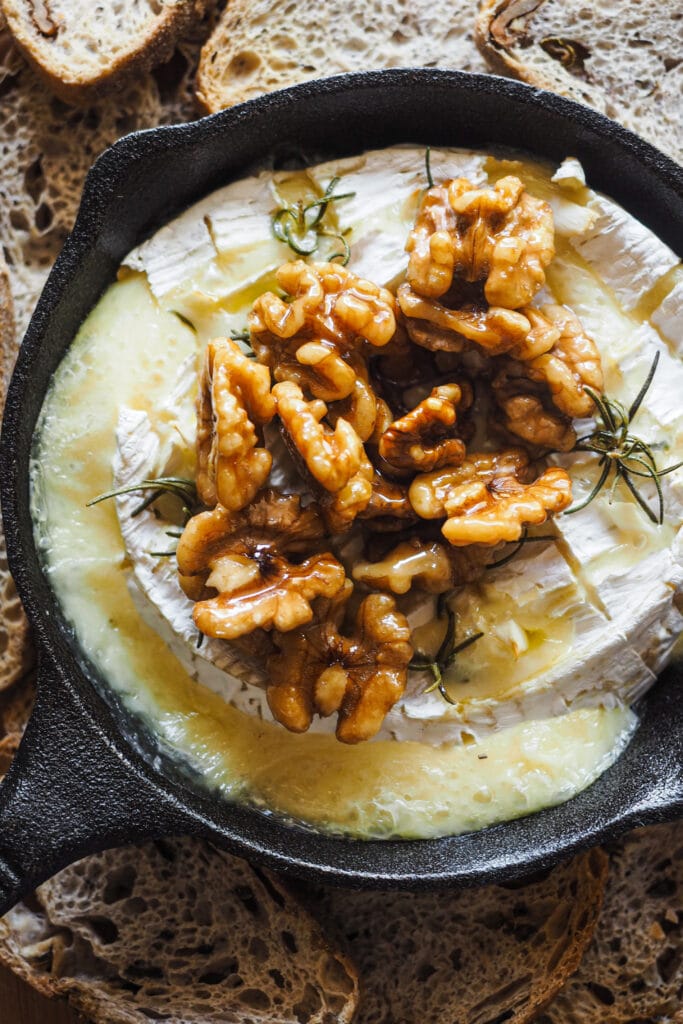 Esta receta de camembert al horno con ajo, romero y nueces caramelizadas es festiva, fácil de preparar y ¡siempre enamora! Rápida, pocos ingredientes y súper deliciosa. El ajo y romero aportan un aroma increíble al Camembert, ya de por si un poco frutal y complejo. Para acompañar, unas tostadas y la guinda del pastel, unas nueces caramelizadas con sirope de arce que también puedes usar para dipear o como acompañamiento de cualquier tabla de quesos y embutidos. | Receta de Paula's Apron