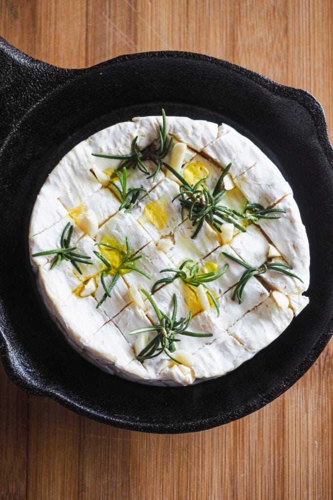 Camembert con romero, ajo y un chorro de aceite de oliva antes de hornearse.