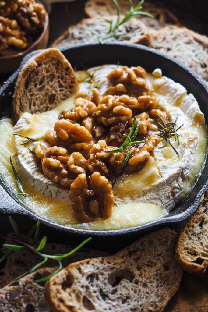 Esta receta de camembert al horno con ajo, romero y nueces caramelizadas es festiva, fácil de preparar y ¡siempre enamora! Rápida, pocos ingredientes y súper deliciosa. El ajo y romero aportan un aroma increíble al Camembert, ya de por si un poco frutal y complejo. Para acompañar, unas tostadas y la guinda del pastel, unas nueces caramelizadas con sirope de arce que también puedes usar para dipear o como acompañamiento de cualquier tabla de quesos y embutidos. | Receta de Paula's Apron
