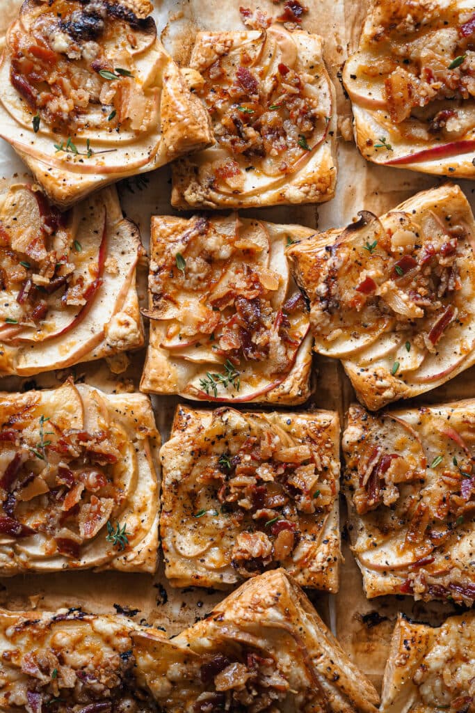 Estos Hojaldritos de Manzana con Panceta y Cheddar son un aperitivo ideal durante otoño e invierno. Mezclan a la perfección dulce y salado, con la manzana de temporada que tan bien le va a la panceta. Y te sorprenderá la combinación, pero un toque de cheddar maduro queda de maravilla, con su punto de sabor un poco salado pero sin ser demasiado fuerte. Son fáciles de hacer y solo llevan 5 ingredientes, ¡simplemente perfectos! | Receta de Paula's Apron