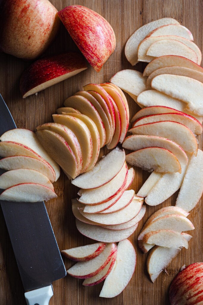 Manzanas laminadas con un cuchillo al lado sobre una tabla de madera.