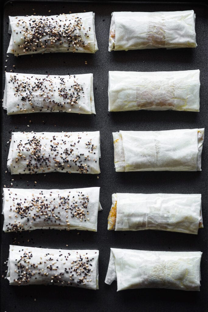 Rollitos Primavera de Verduras con Masa Filo algunos espolvoreados con semillas de sésamo blancas y negras antes de ser horneados. | Receta de Paula's Apron