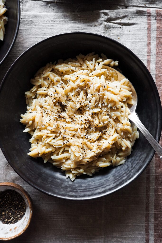Esta receta de Orzo Cacio e Pepe (Orzotto Cacio e Pepe o Falso Risotto de Orzo con Queso y Pimienta) combina los sabores del clásico plato de pasta romano con la textura de un risotto quedando increíblemente bueno y lo mejor de todo es que es fácil y rápido de hacer: se hace todo en una sartén o cazuela sin necesidad de ir removiendo el orzo y todo el caldo se echa de golpe. Para la próxima cena o comida que tengas a tu cargo y en la que quieras impresionar sin complicarte nada, este Orzo Cacio e Pepe es tu receta. | Receta de Paula's Apron
