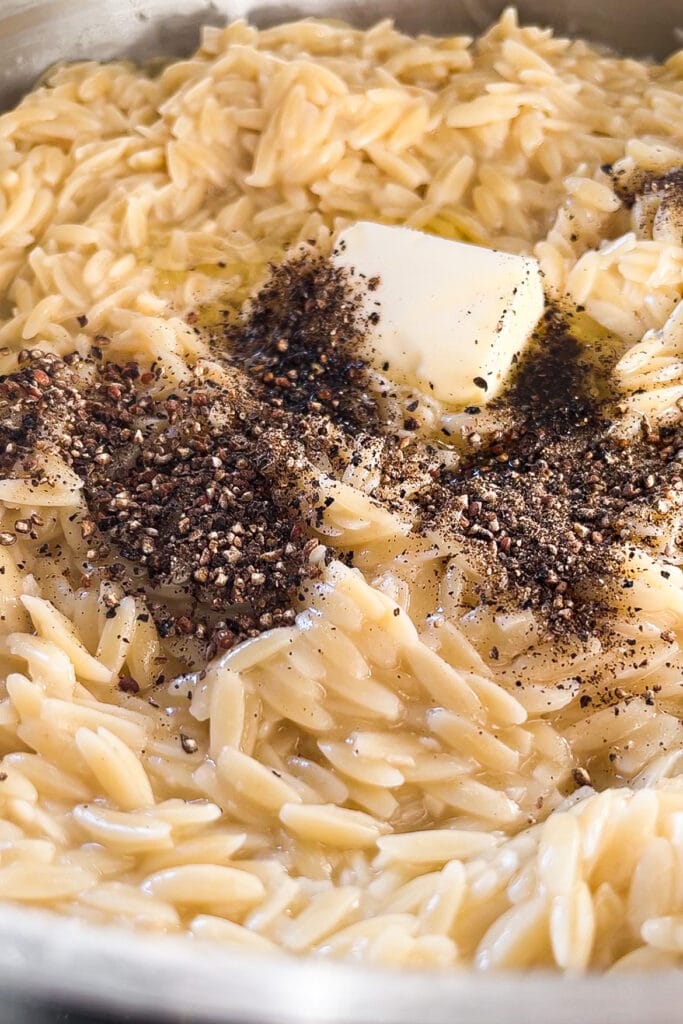 Esta receta de Orzo Cacio e Pepe (Orzotto Cacio e Pepe o Falso Risotto de Orzo con Queso y Pimienta) combina los sabores del clásico plato de pasta romano con la textura de un risotto quedando increíblemente bueno y lo mejor de todo es que es fácil y rápido de hacer: se hace todo en una sartén o cazuela sin necesidad de ir removiendo el orzo y todo el caldo se echa de golpe. Para la próxima cena o comida que tengas a tu cargo y en la que quieras impresionar sin complicarte nada, este Orzo Cacio e Pepe es tu receta. Aquí se puede ver el orzo cremoso con la pimienta y mantequilla encima antes de integrarlo todo bien. | Receta de Paula's Apron