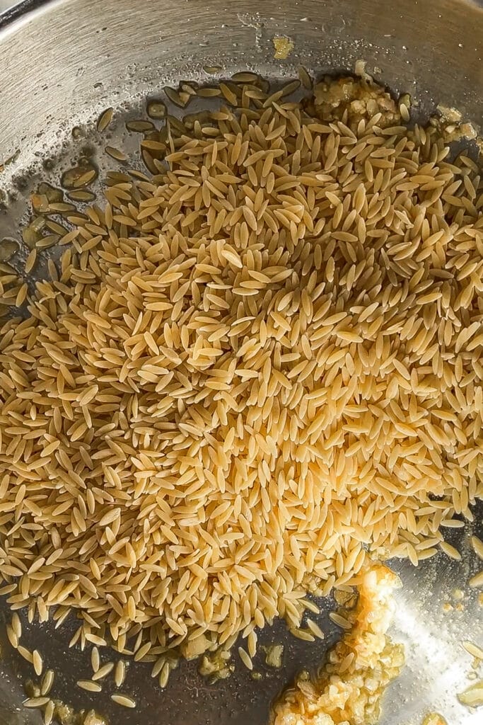 Orzo en una sartén con sofrito de cebolla y ajo.