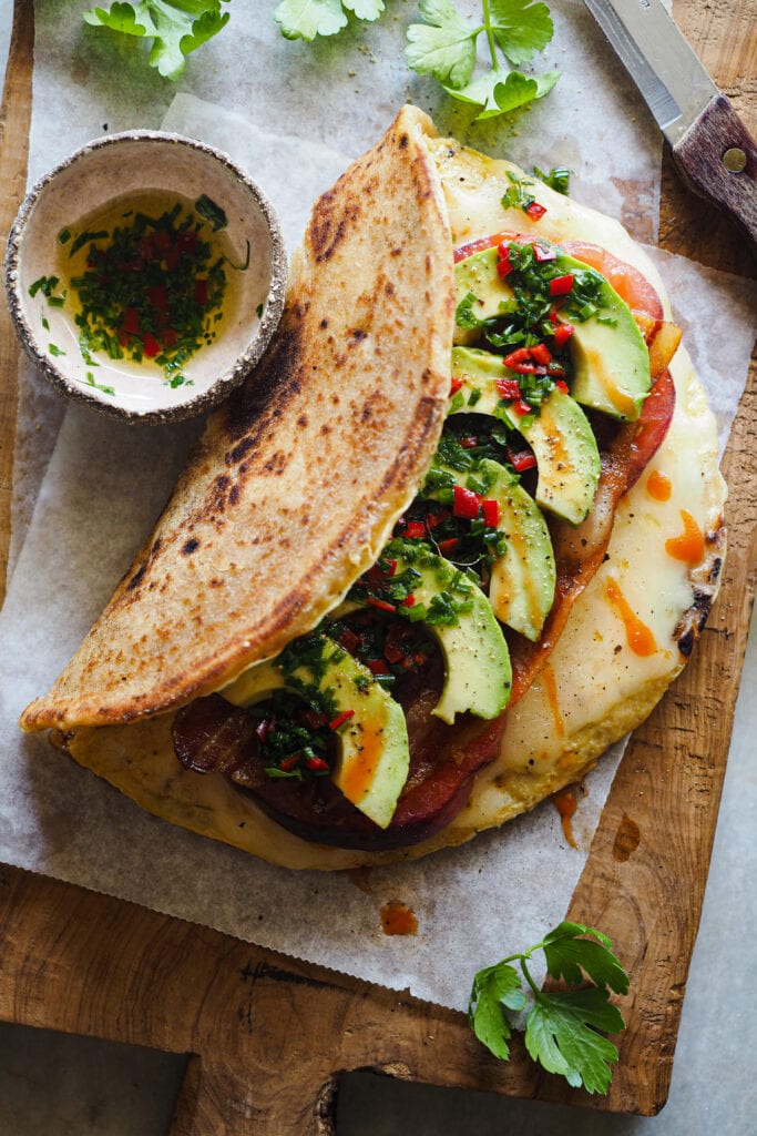Este Bocadillo de Tortilla con Pan Naan, Queso, Aguacate, Tomate y Bacon es súper completo. Queda jugoso y sabroso y lo tienes listo en 10 minutos. Va bien tanto para desayuno o brunch como para una comida o cena rápida y queda buenísimo. Si uno te parece grande, siempre lo puedes partir por la mitad y quedarte con una, aunque te aseguro que a la que le pegues un mordisco no querrás compartir nada. | Receta de Paula's Apron