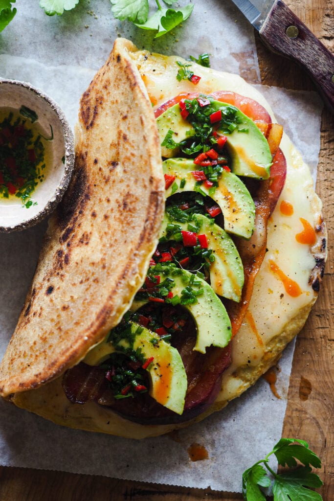 Este Bocadillo de Tortilla con Pan Naan, Queso, Aguacate, Tomate y Bacon es súper completo. Queda jugoso y sabroso y lo tienes listo en 10 minutos. Va bien tanto para desayuno o brunch como para una comida o cena rápida y queda buenísimo. Si uno te parece grande, siempre lo puedes partir por la mitad y quedarte con una, aunque te aseguro que a la que le pegues un mordisco no querrás compartir nada. | Receta de Paula's Apron
