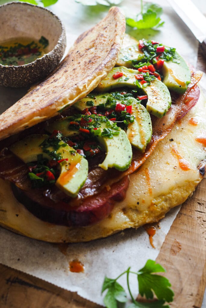 Este Bocadillo de Tortilla con Pan Naan, Queso, Aguacate, Tomate y Bacon es súper completo. Queda jugoso y sabroso y lo tienes listo en 10 minutos. Va bien tanto para desayuno o brunch como para una comida o cena rápida y queda buenísimo. Si uno te parece grande, siempre lo puedes partir por la mitad y quedarte con una, aunque te aseguro que a la que le pegues un mordisco no querrás compartir nada. | Receta de Paula's Apron
