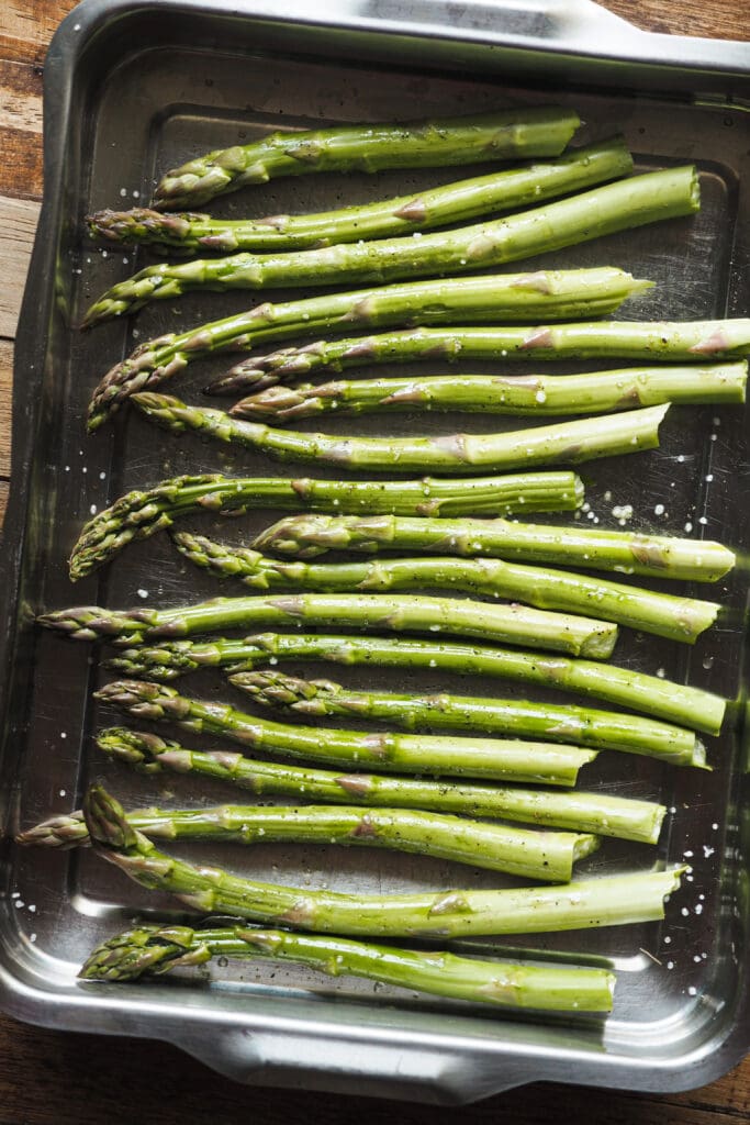 Espárragos salpimentados y con aceite en una bandeja de horno antes de ser horneados.