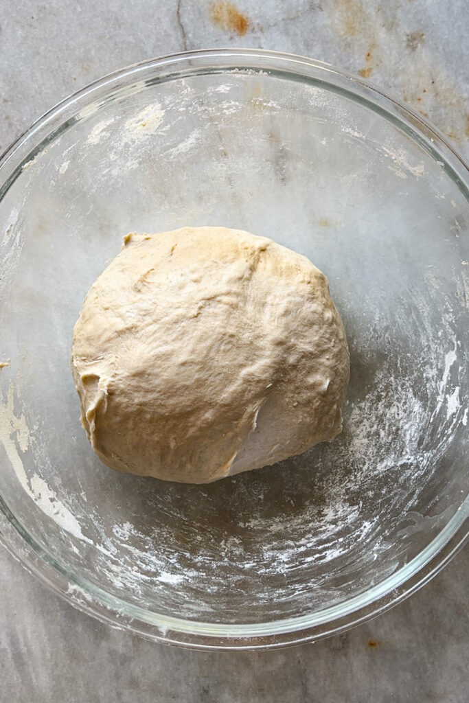 Masa para pan naan en forma de bola en un bol de cristal lista para fermentar.