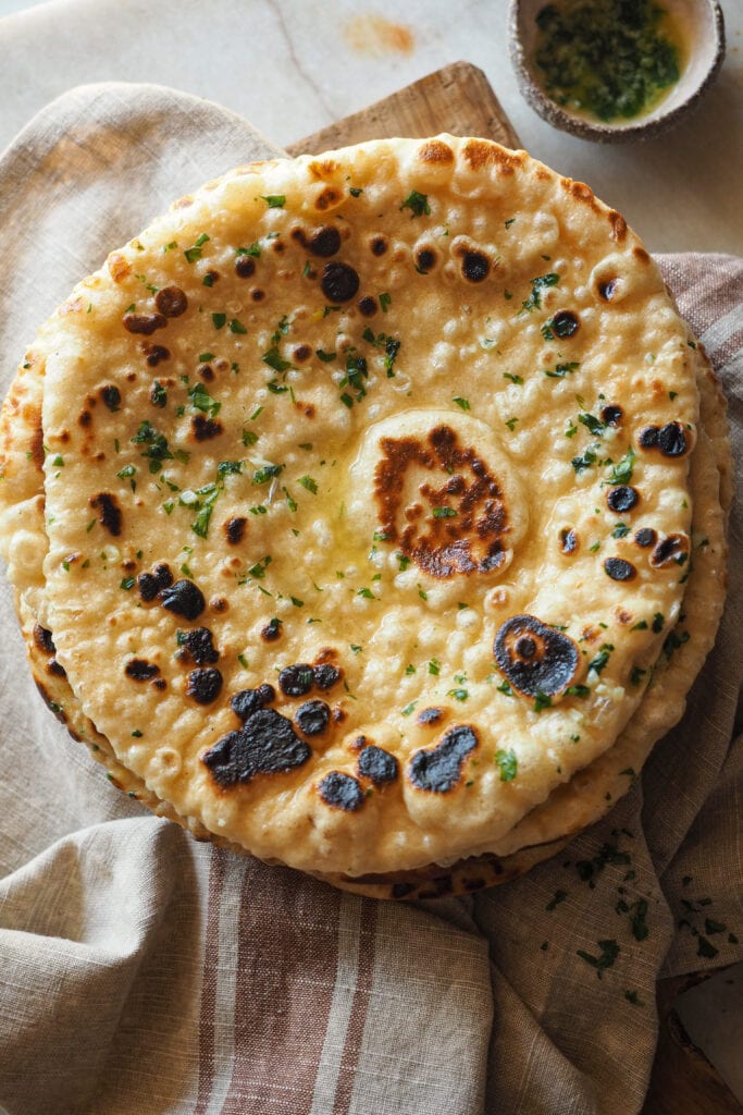 Este Pan Naan Casero queda extra tierno, esponjoso y no necesita de ninguna máquina para amasar. A mi me encanta darle un toque final con mantequilla de ajo y perejil, pero es totalmente opcional. Es una receta de pan naan fácil de hacer (que requiera tiempo de levado no significa difícil :P) y muy poco exigente a la hora de darte un resultado increíble con poco. Sírvelo con tus platos indios favoritos - con cualquier curry está de muerte -, pero también va genial con salsas de yogur, chutneys, hummus o simplemente solo… Recién salido de la sartén ya está de vicio. | Receta de Paula's Apron