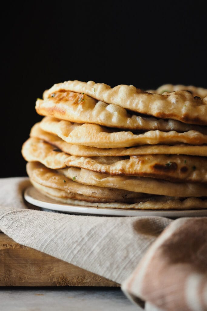 Este Pan Naan Casero queda extra tierno, esponjoso y no necesita de ninguna máquina para amasar. A mi me encanta darle un toque final con mantequilla de ajo y perejil, pero es totalmente opcional. Es una receta de pan naan fácil de hacer (que requiera tiempo de levado no significa difícil :P) y muy poco exigente a la hora de darte un resultado increíble con poco. Sírvelo con tus platos indios favoritos - con cualquier curry está de muerte -, pero también va genial con salsas de yogur, chutneys, hummus o simplemente solo… Recién salido de la sartén ya está de vicio. | Receta de Paula's Apron