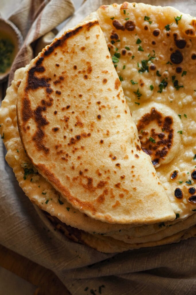 Este Pan Naan Casero queda extra tierno, esponjoso y no necesita de ninguna máquina para amasar. A mi me encanta darle un toque final con mantequilla de ajo y perejil, pero es totalmente opcional. Es una receta de pan naan fácil de hacer (que requiera tiempo de levado no significa difícil :P) y muy poco exigente a la hora de darte un resultado increíble con poco. Sírvelo con tus platos indios favoritos - con cualquier curry está de muerte -, pero también va genial con salsas de yogur, chutneys, hummus o simplemente solo… Recién salido de la sartén ya está de vicio. | Receta de Paula's Apron