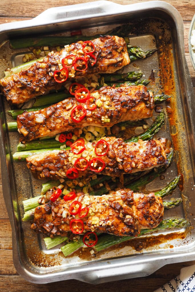 Este Salmón al Horno con Espárragos y Vinagreta de Miel y Limón es fresco, ligero, fácil de hacer y nutritivo, ¡lo tiene todo! El salmón se marina con una vinagreta deliciosa que mezcla un toque ácido con dulce y salado. Luego se cocina todo junto en una bandeja de horno y terminamos con un topping de chile y cebolleta. Sírvelo con arroz o puré de patatas y tienes un plato completo para una comida saludable, o acompáñalo de ensalada si quieres algo más light para la cena. ¡Una delicia! | Receta de Paula's Apron