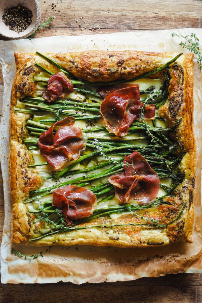 Celebra la Primavera con este Hojaldre de Espárragos y Brie con Jamón y Pesto fácil y sobre todo delicioso. Y es que cuando combinas una verdura ya de por si buena con queso, crujiente y el toque saladito del jamón, te explota la cabeza. Además, para la base del hojaldre he usado pesto, el cual combina a la perfección con el resto de ingredientes y el aroma de la albahaca aporta frescura. Si sirves este hojaldre en el próximo aperitivo, comida o cena del que te encargues, te prometo que vas a triunfar. | Receta de Paula's Apron