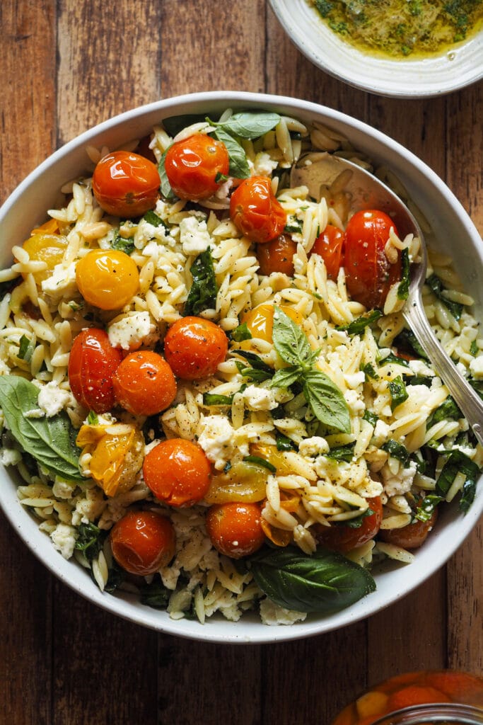 Ensalada de Orzo con Tomate Confitado y Feta en 15 minutos y llenas de sabor con solo 4 ingredientes principales. La gracia está en aprovechar todos los elementos del tomate confitado (aceite, ajo y chalota, además del tomate) para aportar el máximo sabor a una ensalada con muy pocos ingredientes: pasta, espinacas para un toque verde, el tomate confitado, feta y el aliño, la magia de esta ensalada de pasta. La puedes servir fría o tíbia, de ambas formas está buenísima, por lo que te recomiendo que, si la preparas, hagas en cantidad así tienes para otro día. | Receta de Paula's Apron