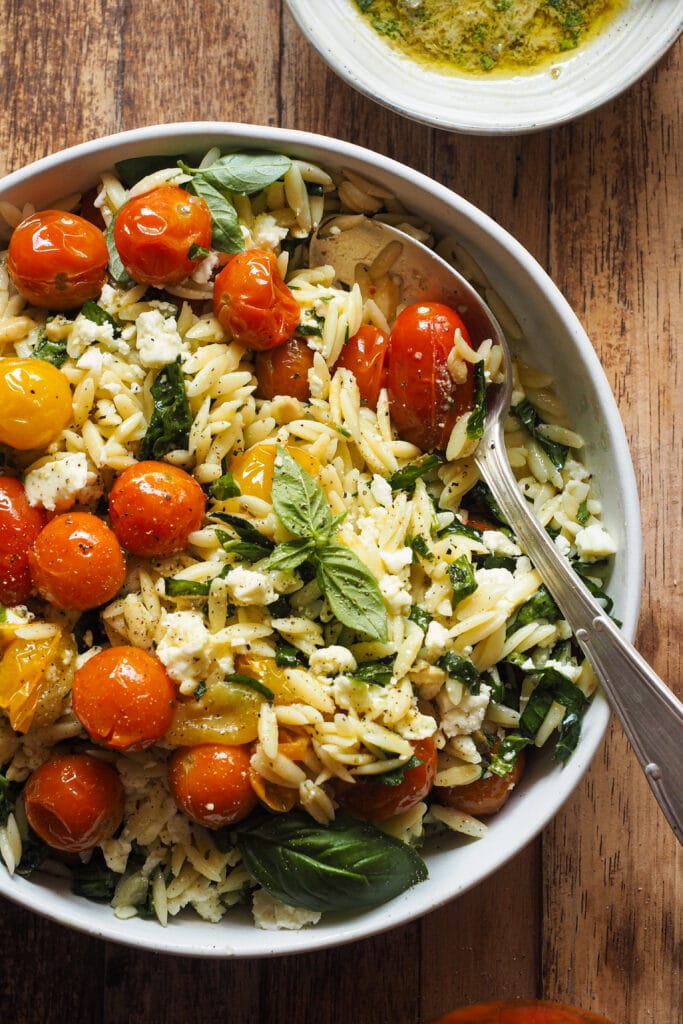 Ensalada de Orzo con Tomate Confitado y Feta en 15 minutos y llenas de sabor con solo 4 ingredientes principales. La gracia está en aprovechar todos los elementos del tomate confitado (aceite, ajo y chalota, además del tomate) para aportar el máximo sabor a una ensalada con muy pocos ingredientes: pasta, espinacas para un toque verde, el tomate confitado, feta y el aliño, la magia de esta ensalada de pasta. La puedes servir fría o tíbia, de ambas formas está buenísima, por lo que te recomiendo que, si la preparas, hagas en cantidad así tienes para otro día. | Receta de Paula's Apron