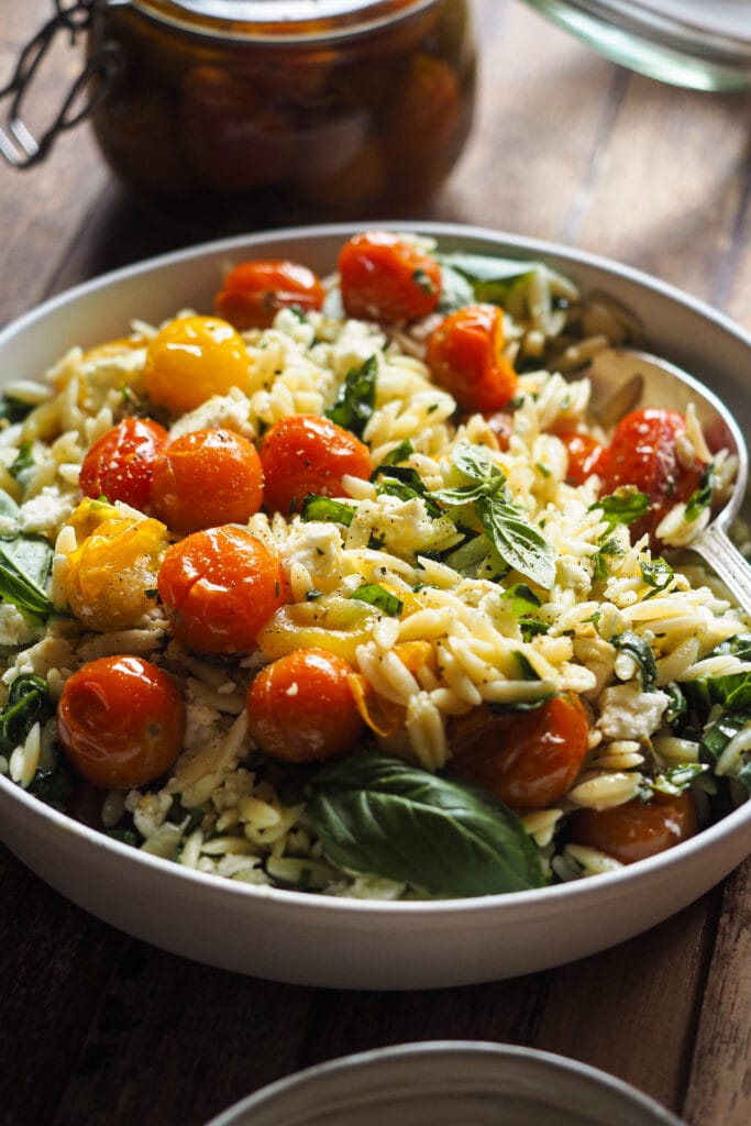 Ensalada de Orzo con Tomate Confitado y Feta en 15 minutos y llenas de sabor con solo 4 ingredientes principales. La gracia está en aprovechar todos los elementos del tomate confitado (aceite, ajo y chalota, además del tomate) para aportar el máximo sabor a una ensalada con muy pocos ingredientes: pasta, espinacas para un toque verde, el tomate confitado, feta y el aliño, la magia de esta ensalada de pasta. La puedes servir fría o tíbia, de ambas formas está buenísima, por lo que te recomiendo que, si la preparas, hagas en cantidad así tienes para otro día. | Receta de Paula's Apron