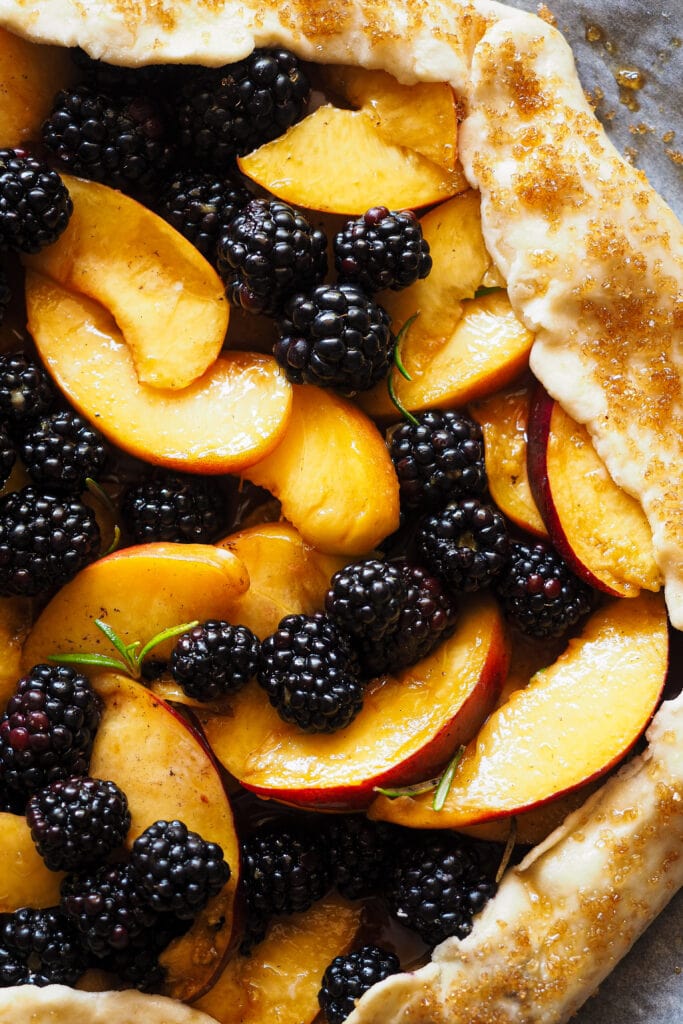 Galette de Nectarina y Moras al Romero sin hornear desde cerca: se ve el relleno de nectarina, moras y romero y el borde pincelado con huevo y espolvoreado con azúcar.