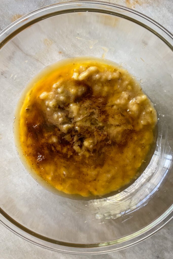 3 plátanos maduros chafados en un bol de cristal con mantequilla tostada y aceite de girasol sin mezclar.