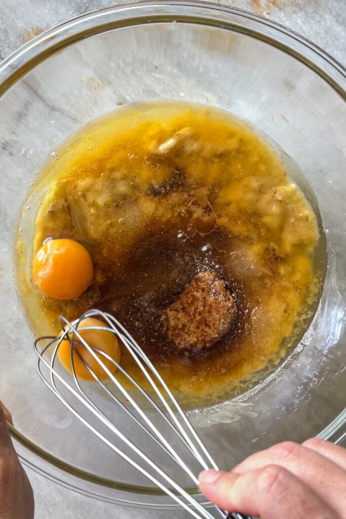 3 plátanos maduros chafados en un bol de cristal con mantequilla tostada, aceite de girasol, azúcar moreno, azúcar blanco y 2 huevos sin mezclar.