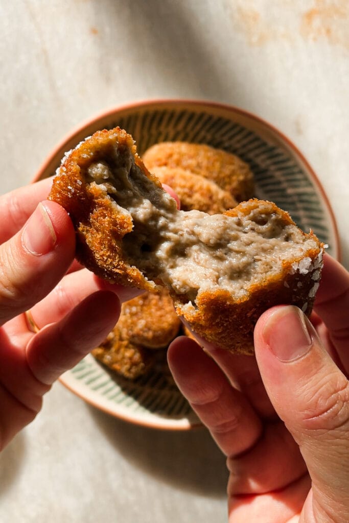Croquetas de Setas cremosas por dentro y crujientes por fuera, con un increíble sabor umami gracias al boletus. Tamnbién llevan champiñones y te explico como hacer la bechamel perfecta para que no queden grumos. Estas croquetas son un homenaje al otoño e ideales para un buen picoteo o aperitivo. En esta foto se puede ver como parto una croqueta en dos y lo cremoso que es su interior. | Receta de Paula's Aspron