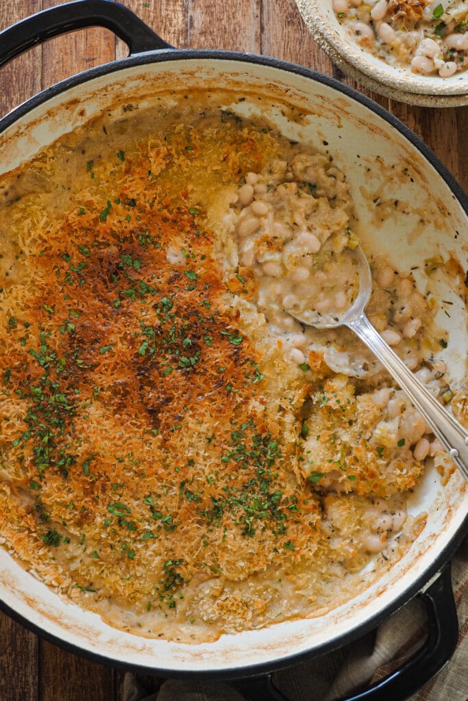 Esta receta de Gratén de Alubias y Puerro es una forma diferente y buenísima de disfrutar de esta legumbre. Es fácil de hacer y como resultado te quedan unas alubias suaves con una salsa extra cremosa que contrasta con el crujiente del gratinado. Otra cosa que me encanta es que se prepara en 15 minutos y el resto lo hace el horno, lo que encima te permite prepararlas con antelación y meterlas al horno cuando vayas a comer. En definitiva, un plato súper completo en todos los sentidos e ideal para entrar en calor estos meses fríos. | Receta de Paula's Apron