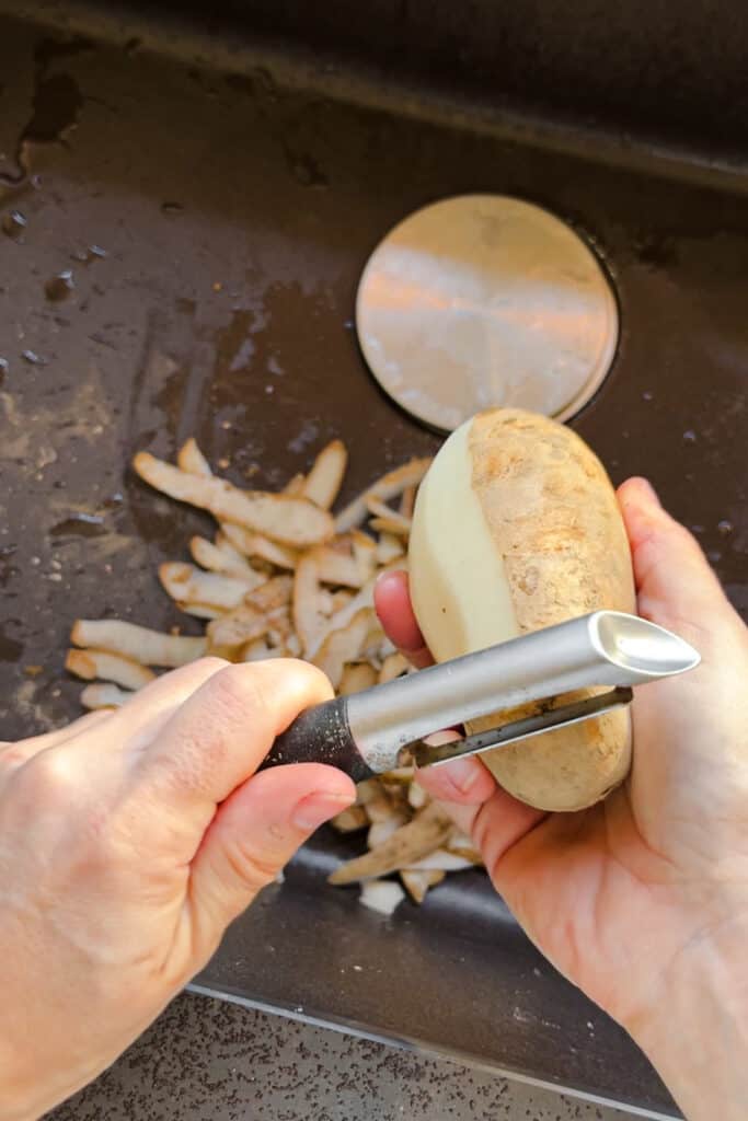 Pelando patatas para hacer puré de patatas encima del fregadero de la cocina.