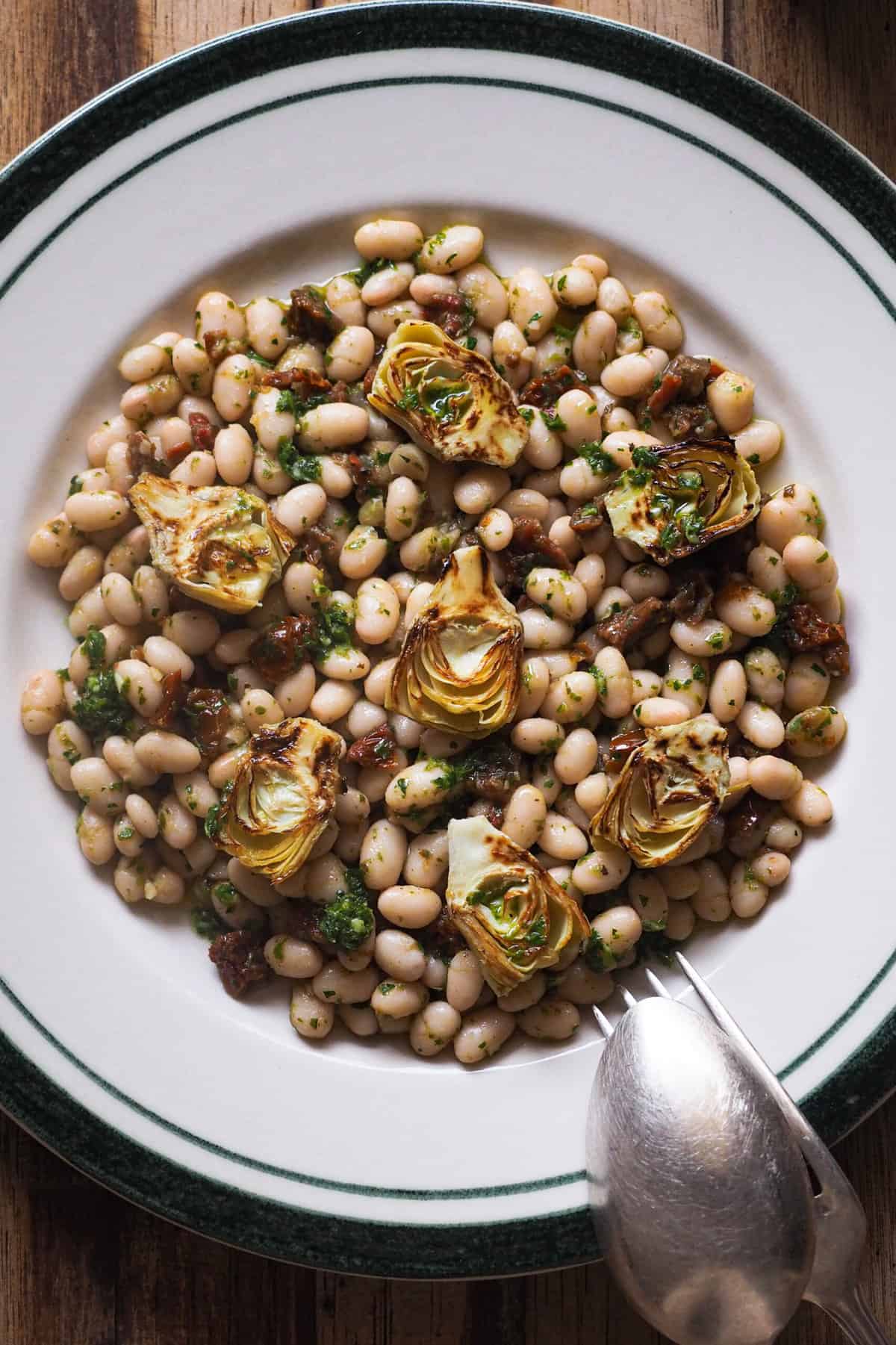 Ensalada de Alubias con Tomate Seco y Alcachofa súper sabrosa y lista en menos de 10 minutos. Es ideal para hacer modo batchcooking, si tienes que prepararte comida en un pispas o para llevar en tupper el día siguiente, solo pide 3 ingredientes y un buen aliño. Hoy he tirado de mi salsa verde porque tenía una bote en la nevera, pero puedes usar pesto o un simple majado de ajo y perejil. Uses lo que uses, te queda una ensalada ideal en un abrir y cerrar de ojos. | Receta de Paula's Apron