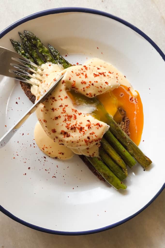 Huevo escalfado con espárragos y salsa holandesa fácil sobre una tostada. El huevo escalfado está cortado y la yema líquida se mezcla con la salsa holandesa. | Receta de Paula's Apron