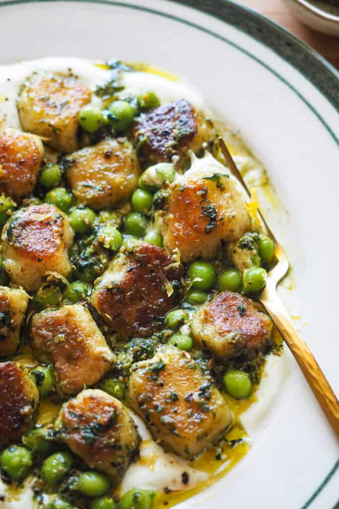 Estos Ñoquis con Pesto de Pistachos, Guisantes y Crema de Ricotta son puro contraste de sabores y texturas además de ligeros a la vez que saciantes. El pesto le da un toque de frescura, la textura de los guisantes contrasta con la de los ñoquis extra suaves y esponjosos y la crema de ricotta es el componente que lo une todo con su cremosidad y toque de limón. Un plato de restaurante en casa. | Receta de Paula's Apron