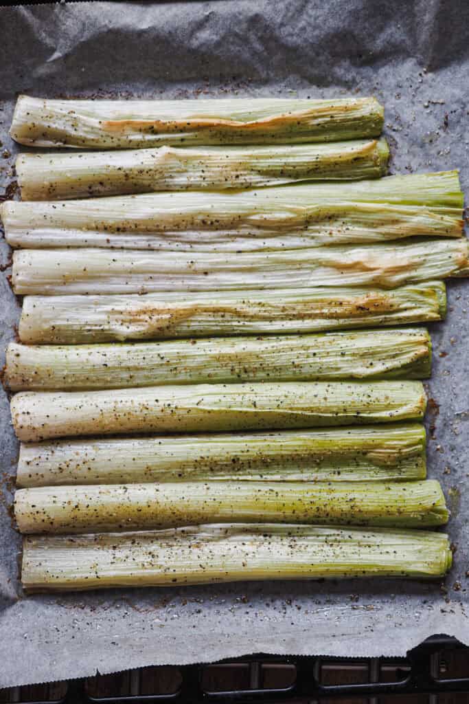 Puerros asados sobre bandeja de horno con aceite, sal y pimienta negra.