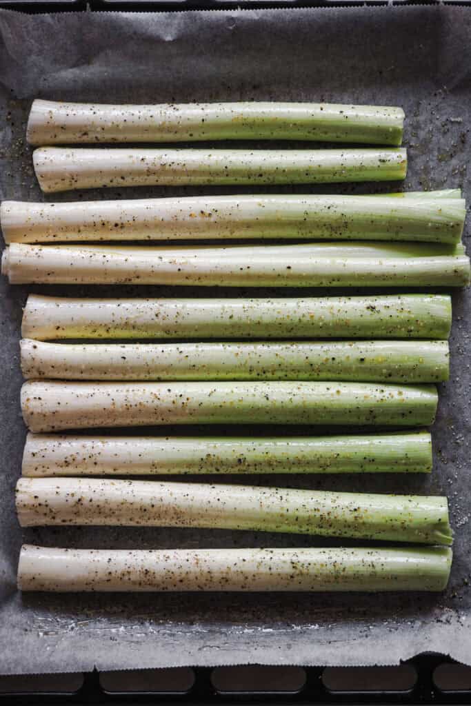 Puerros crudos sobre bandeja de horno con aceite, sal y pimienta negra.
