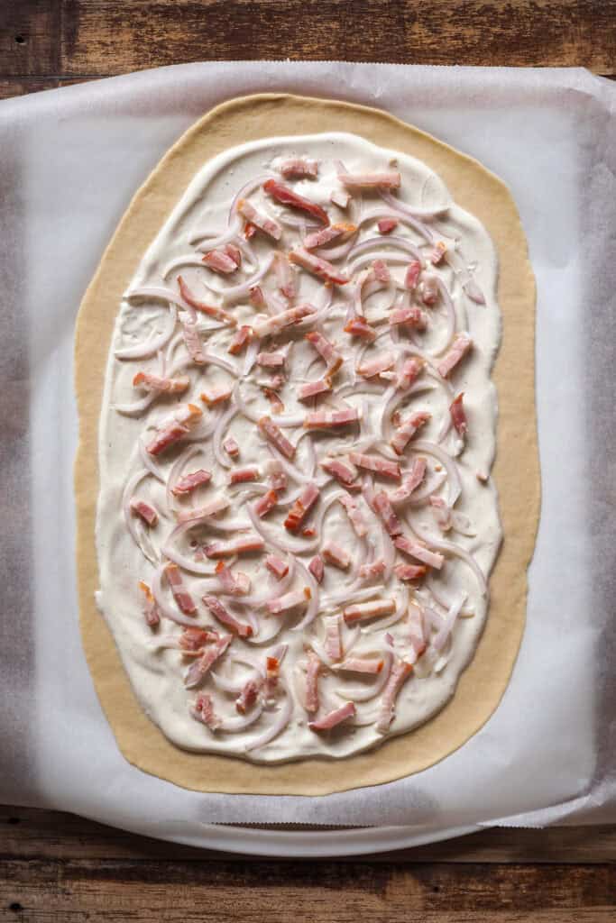 Paso 3 Flammkuchen: panceta repartida por encima de cebolla finamente cortada y de la base de crème fraîche.